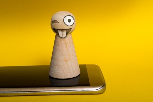 Pawn with mad emoji face standing on smartphone