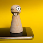 Pawn with mad emoji face standing on smartphone
